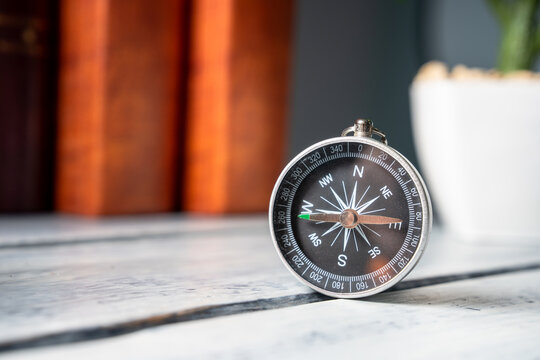 A compass lying on a table against a background of books