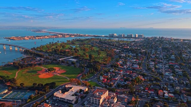 Aerial view of Coronado neighborhoods and coastal recreation grounds. Homes border baseball fields, tennis courts and a golf course, with the bay and ocean beyond.