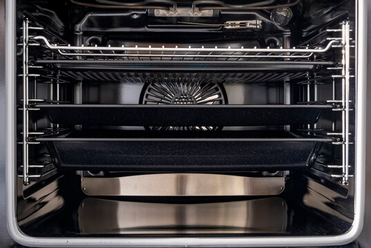 Symmetrical interior view of a modern electric oven featuring multiple baking trays and a convection fan. Showcases high-end stainless steel construction and organized storage racks.