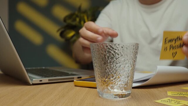 Man sticks an &ldquo;Everything Is Possible&rdquo; motivational note onto a glass and then continues working on his laptop at the desk.
