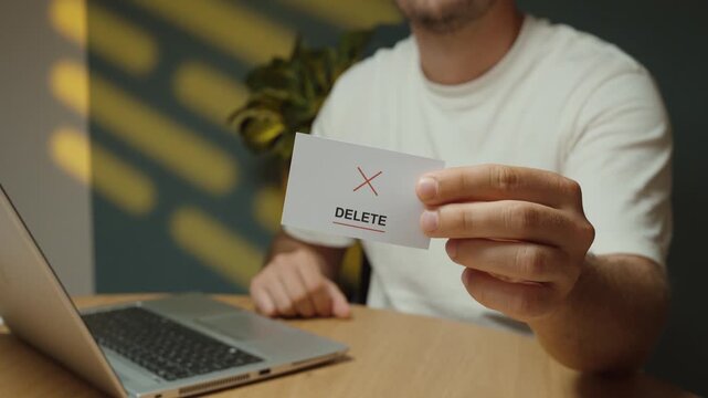 Man flips a small card to reveal a &ldquo;Delete&rdquo; message with red cross symbol, representing data removal, deleting files and digital cleanup.
