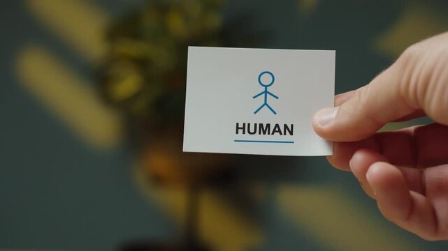 Hand flips a small card to reveal a &ldquo;Human&rdquo; message with person symbol, representing human verification, online authentication and distinguishing people from automated bots