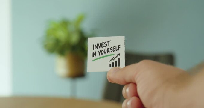 Close-up of a hand holding an &ldquo;Invest in Yourself&rdquo; card with growth chart, representing personal development, career growth and self-improvement.