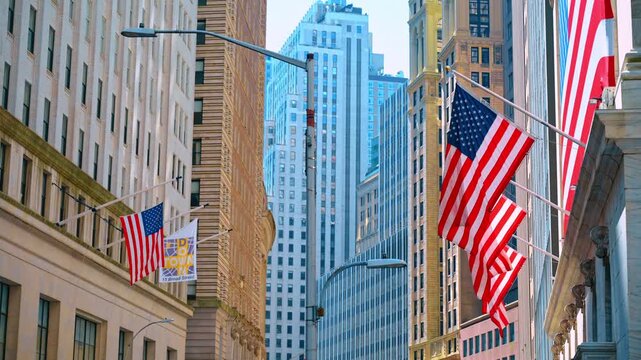 American flags along Broad Street between Manhattan buildings. Red and white stripes hang from angled poles among stone facades, windows and streetlights.