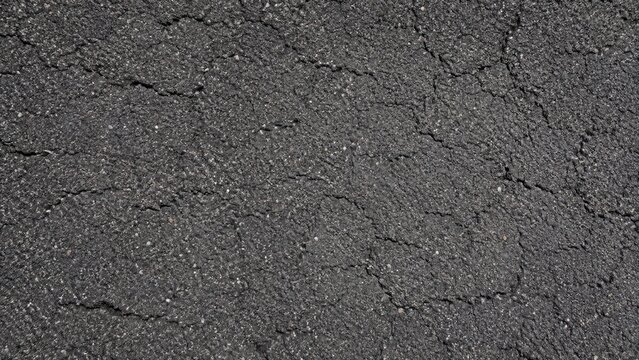 Close-up of cracked asphalt road surface showing textured dark pavement and granular aggregate