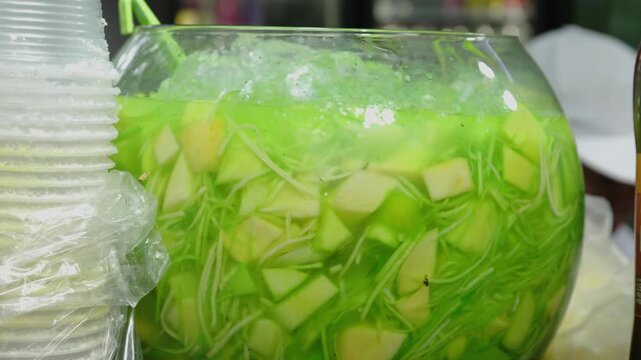 Large glass bowl filled with traditional green sour mango biche drink and ice, 4k 60fps video.