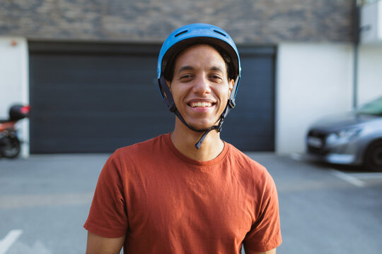 Man Wearing a Blue Helmet, Smiling Broadly in Front of a Garage