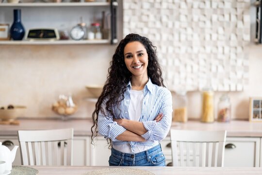 Smiling Young Middle Eastern Woman In Casual Attire Standing With Arms Crossed In Modern Kitchen, Exuding Confidence And Positivity. Embracing Home Lifestyle While Showcasing A Welcoming Environment.
