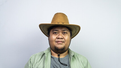 A young male wearing a brown cowboy hat stands facing the camera with a neutral expression against a plain light gray background. The individual is dressed in a grey t-shirt under © M. Faisal Riza