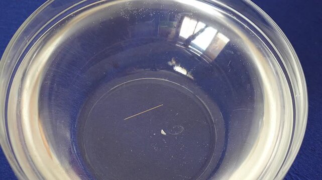 Metal sewing needle floating in water in a glass container.