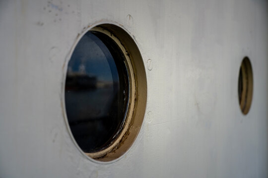 Round glass portholes on white metal ship hull exterior, representing maritime navigation, vessel architecture, nautical travel, and passenger cabin window design.