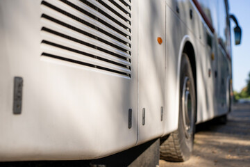 Ventilation cooling grille on rear engine compartment and wheel of white passenger tour bus parked outdoors in sunny day. © Marina