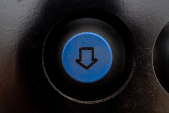 Close up of round blue push button with downward arrow symbol mounted on black control dashboard of heavy industrial or agricultural machine.