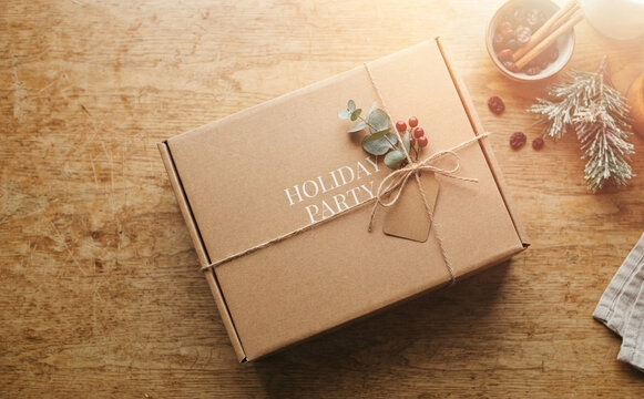 Wrapped holiday party cardboard gift box on a rustic wooden table with festive decoration and twine
