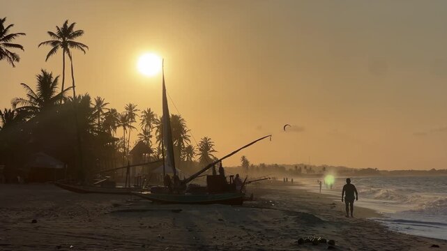 Traditional sailboat and palm trees silhouetted at sunset on Cumbuco Beach, Ceara, Brazil
