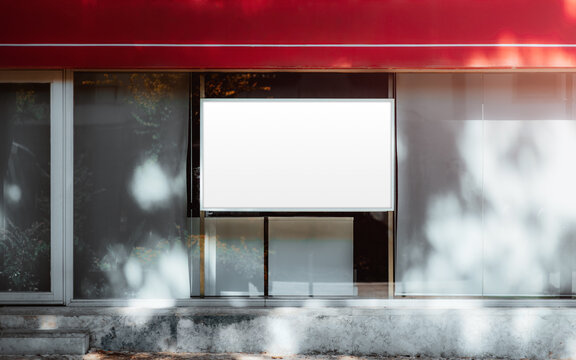 Blank horizontal advertising template displayed inside a glass storefront window beneath a red awning, with soft tree reflections and sunlight framing the clean layout