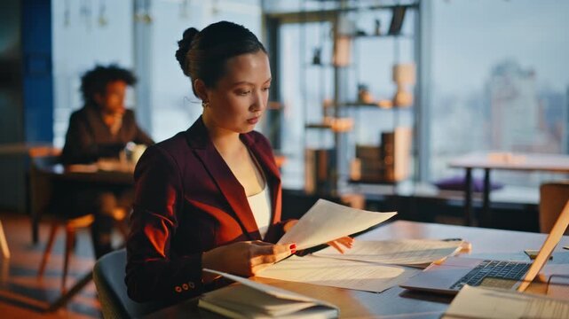 Office worker reviewing papers evening. Asian executive reading contract desk.