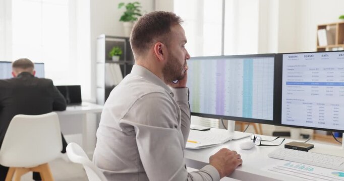 Operator agent handles customer support service by phone. In a modern office he works at a computer with dual monitors displaying spreadsheets and reports. Key customer support office concept.