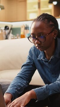 Vertical screen: Uncertain young woman frowns about ambiguous tasks while working remotely on laptop at home, confused about her telecommuting job indoors.