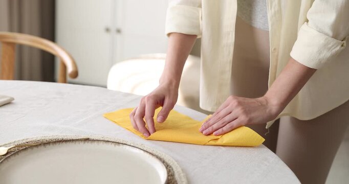 Woman folding yellow napkin and arranging cutlery at table, closeup. Camera tracking and moving forward