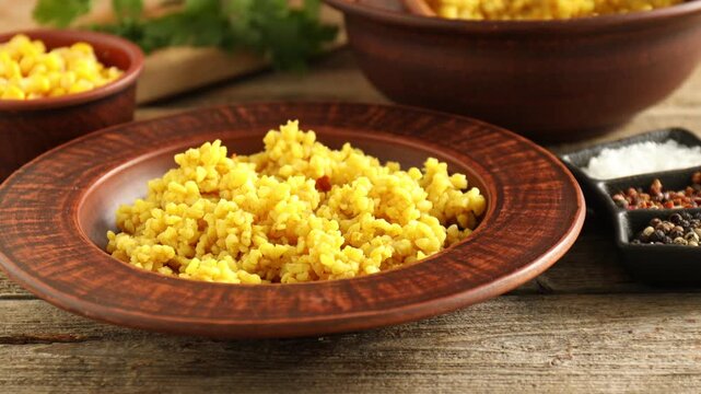Woman adding corn kernels and parsley to delicious bulgur at wooden table, closeup