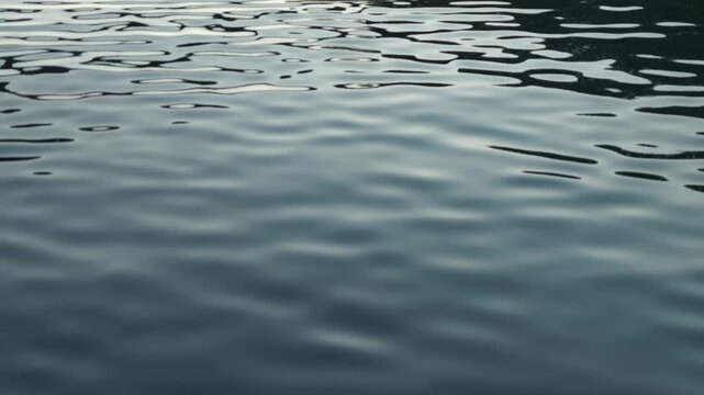 A tranquil, dark water surface gently rippling with soft waves and light reflections in France