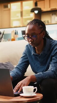 Vertical composition: Young woman cracks knuckles from nervous habit while focused on laptop tasks at home, making repetitive popping sounds during telecommuting work.