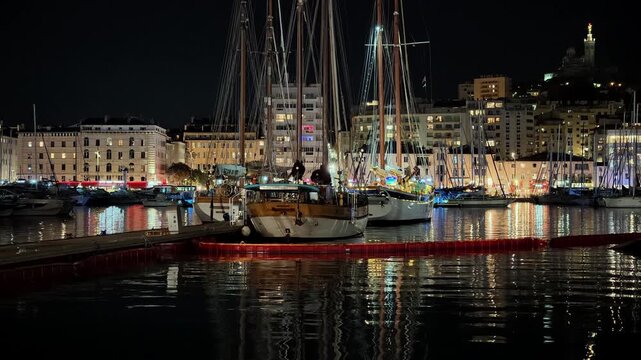 Old sailboats moored at the Vieux Port of Marseille in France with city lights reflecting in the water