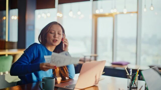 Asian manager talking phone reviewing charts office. Colleague passing document.
