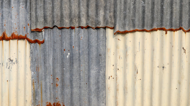 Weathered corrugated metal wall with faded cream and rusty steel panels
