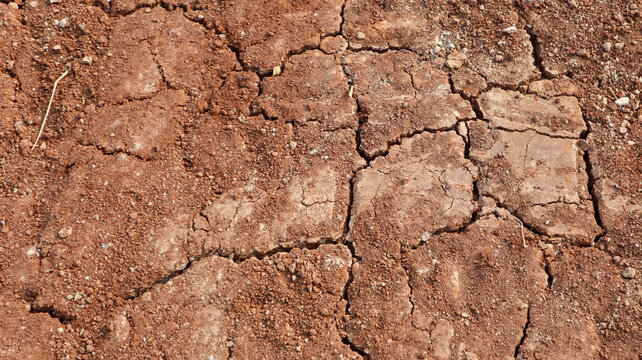 High angle close-up of dry cracked reddish-brown clay soil texture