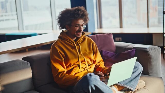 Freelancer typing laptop office sofa. Smiling remote worker coworking space.