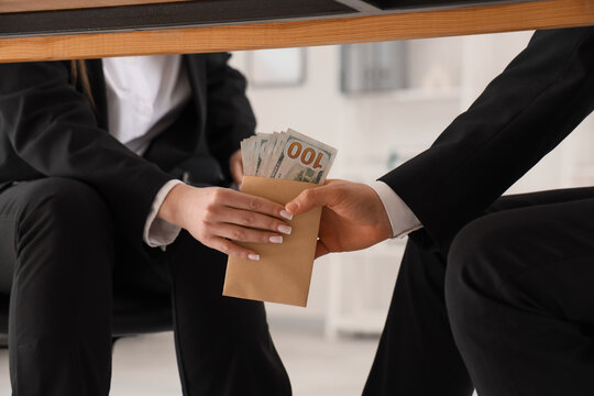 Bribery and corruption in business, person handing over a brown envelope filled with cash to a colleague under a desk in a corporate office environment