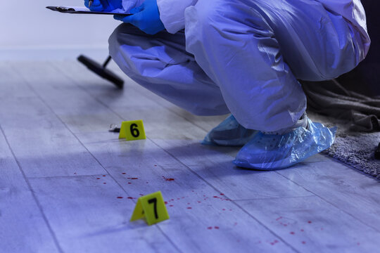 Forensic investigation and crime scene analysis, investigator collecting evidence with blood stains and markers on floor in residential home