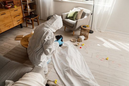 Forensic investigation and crime scene analysis, criminalist in protective suit photographing evidence and body in a residential living room interior