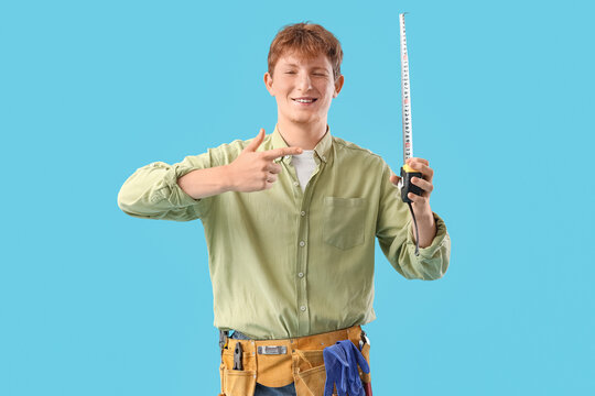 Young man pointing at measuring tape on blue background