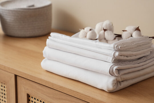 White bed sheets with cotton flowers on chest of drawers in room