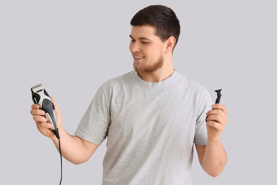 Young bearded man with trimmer and razor on light background