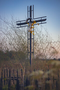 Wayside shrine with Christian metal cross in rural Polish field during dusk
