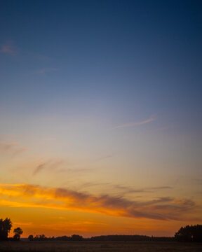 Vibrant twilight sky with orange cirrus clouds over rural landscape silhouette
