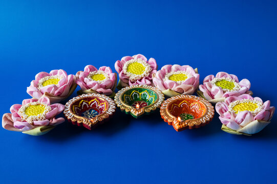 Diwali festival arrangement of glowing diya lamps and pink lotus flowers on a vibrant blue background.