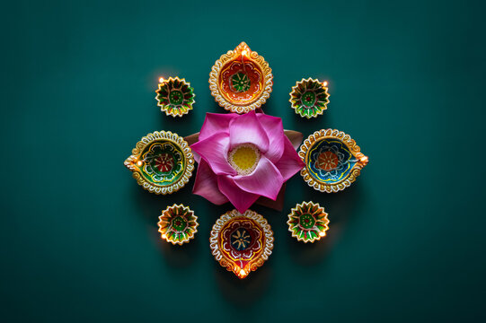 Diwali festival flat lay with a pink lotus flower and glowing diya lamps on teal background.