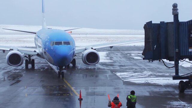Ground Crew Marshaller Guides Passenger Aircraft Near Boarding Bridge At Snowy Ushuaia Airport - 4K