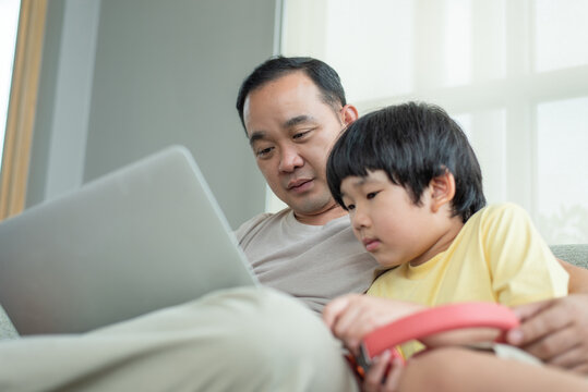 Asian father and little son using laptop computer together at home. Family lifestyle, online education, and technology concept. Human-created, not AI.