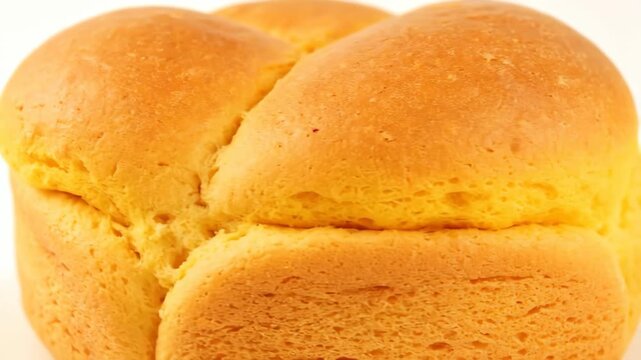 Close-up detail of a freshly baked, golden brown loaf of sweet bread or brioche, showcasing the soft crust and delicious texture against a clean white backdrop.