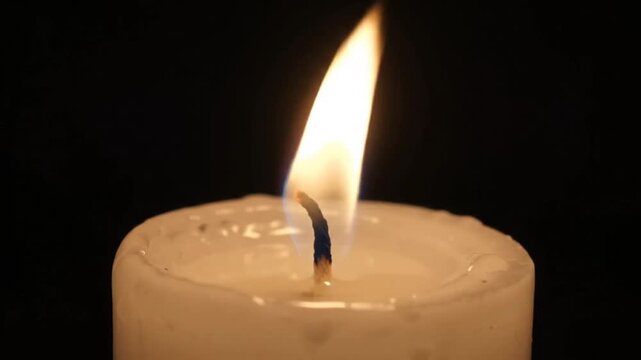 White wax candle burning in the dark with a flickering flame blowing