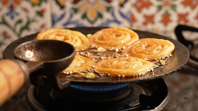 Close up video footage of traditional Indian sweet jalebi frying in hot oil on a gas stove pan during diwali food preparation process for cultural and culinary video projects.
