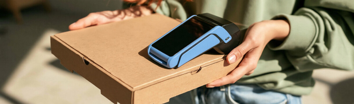 Contactless Pizza Delivery: A person holding a pizza box with a payment terminal on top, ready for a quick and safe contactless transaction.