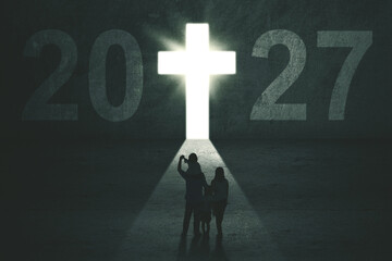 Family Standing Before Glowing Cross and 2027 Numbers on Wall © Creativa Images