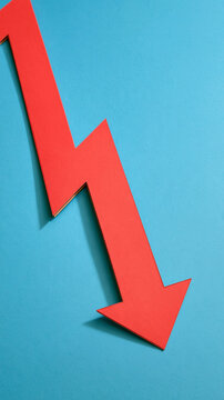 Red Arrow Downwards: A stark red arrow points sharply downwards against a vibrant blue background, symbolizing a decline or downturn in trends, finance, or progress.
